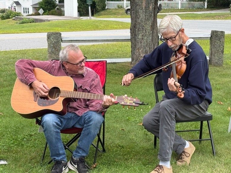 Två män spelar akustisk gitarr och fiol tillsammans utomhus